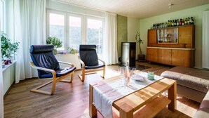 A living room with wooden flooring, two chairs, a sofa, a wooden table, a cabinet with bottles, and a window with curtains. - Holiday Home 'S'Lähmes Auf Der Schwend' with Mountain View, Private Terrace & Wi-Fi (Waldulm)