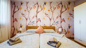 Un lit double avec une couvre-lit à motifs, deux lampes de chevet, une tête de lit en bois et une fresque murale représentant des oiseaux et des feuilles.