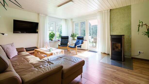 A living room with a sofa, chairs, a TV, a fireplace, and large windows. - Holiday Home 'S'Lähmes Auf Der Schwend' with Mountain View, Private Terrace & Wi-Fi (Waldulm)