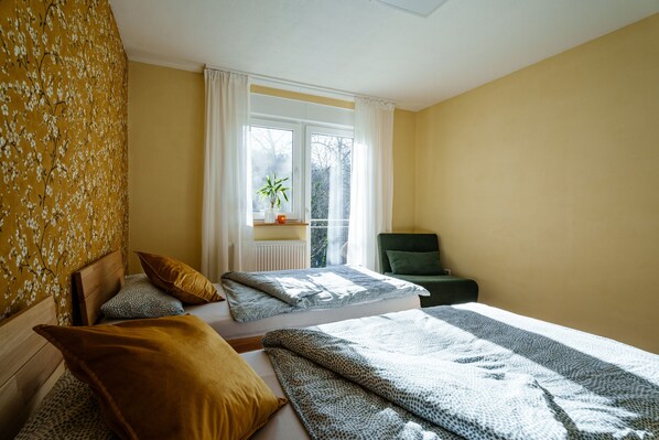 Una habitación con dos camas, una ventana con vistas, una silla y una planta.