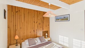 Un dormitorio con cabecera de madera, cama con manta a rayas, lámparas de noche y un cuadro en la pared.