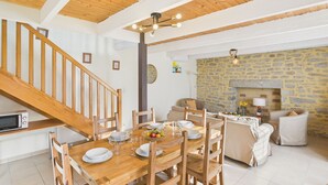 Un comedor con una mesa de madera dispuesta para cuatro, rodeada de sillas de madera. Se observa una pared de piedra y una chimenea al fondo.