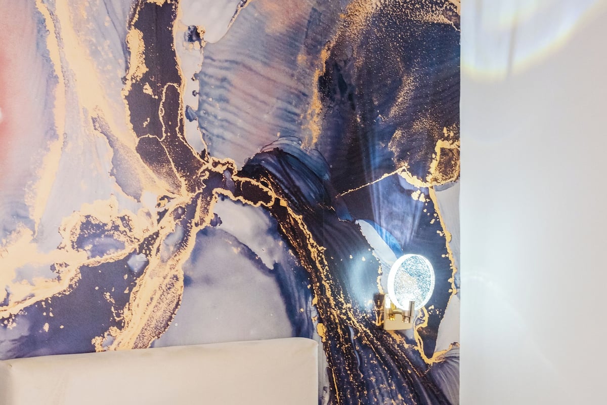 A hotel room with a bed, a wall with a large abstract painting, and a night light.
