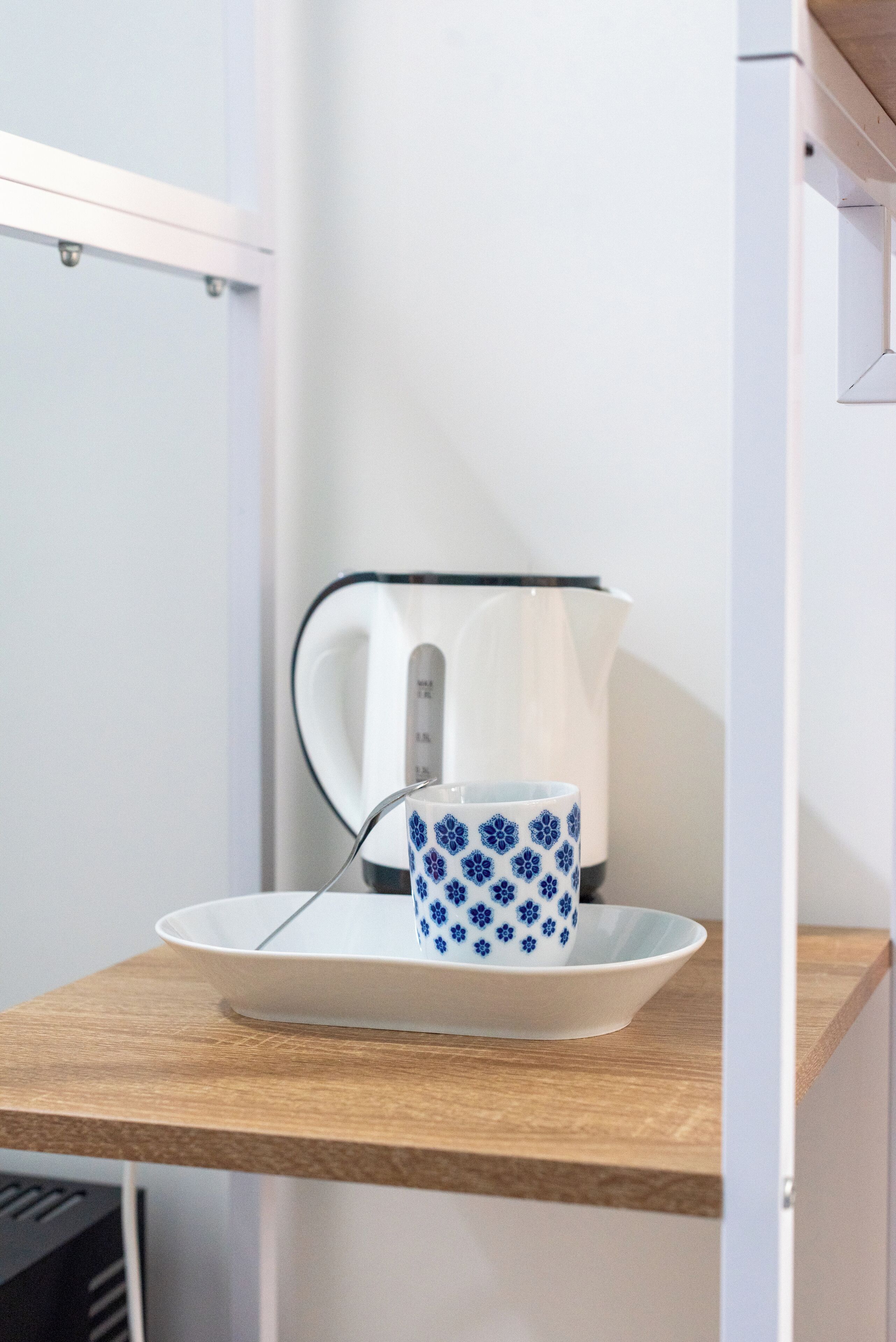 Una cocina con encimera de madera, un hervidor blanco, una taza con diseño azul y un plato blanco.