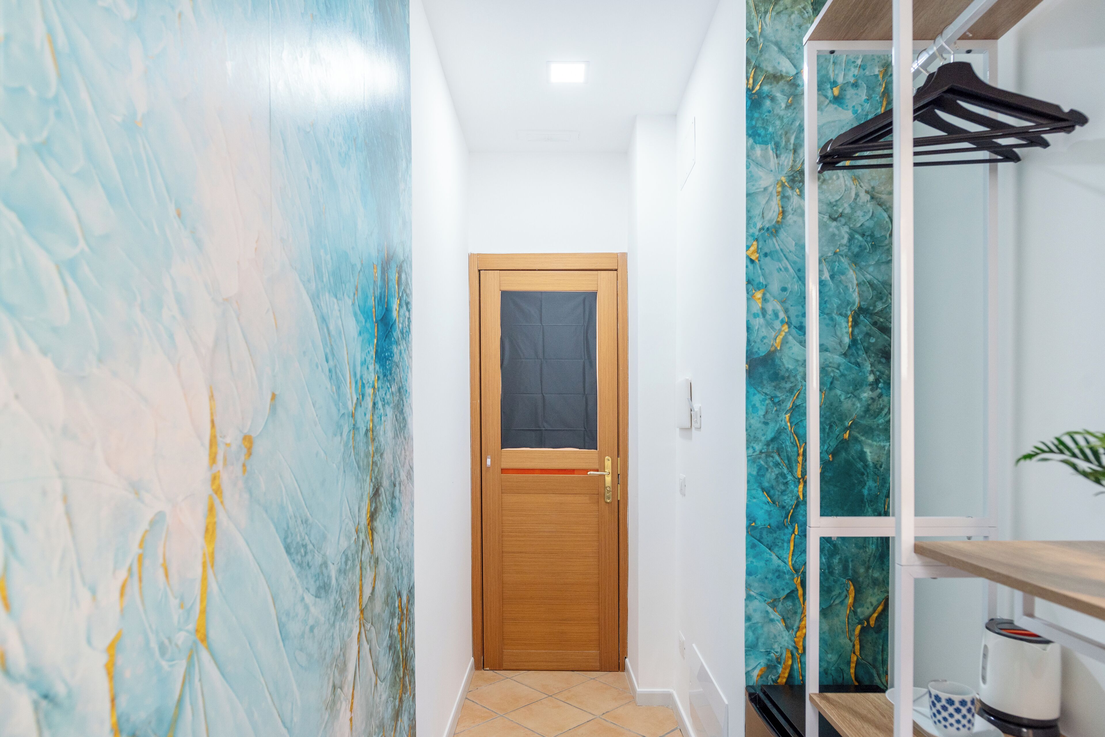 Um corredor com porta de madeira, piso ladrilhado e parede com design abstrato em azul e amarelo.