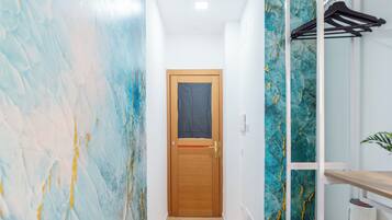 Um corredor com porta de madeira, piso ladrilhado e parede com design abstrato em azul e amarelo.