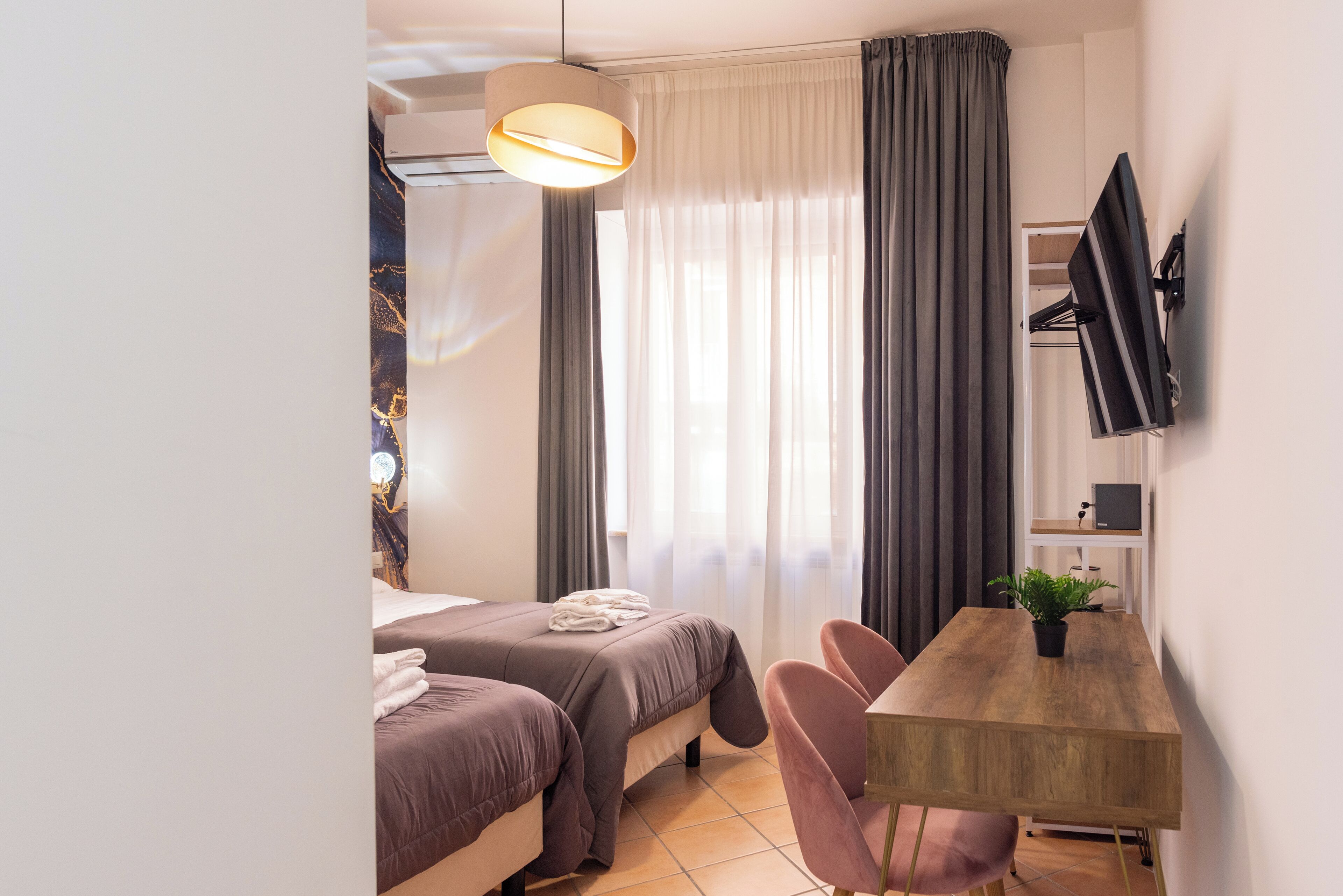 Quarto de hotel moderno com duas camas, uma mesa de jantar de madeira, televisão na parede e uma janela grande com cortinas.