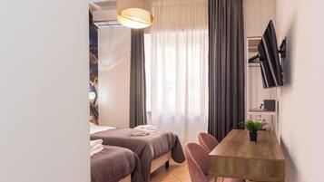 Quarto de hotel moderno com duas camas, uma mesa de jantar de madeira, televisão na parede e uma janela grande com cortinas.