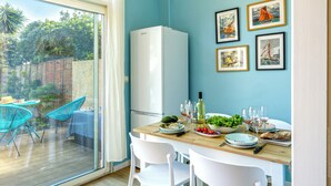 Un comedor con una mesa de madera dispuesta para cuatro personas, sillas blancas y un refrigerador blanco.