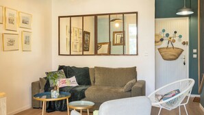 Una sala de estar moderna con un sofá, un sillón y una mesita. Hay cuadros enmarcados en la pared y una cesta colgante.