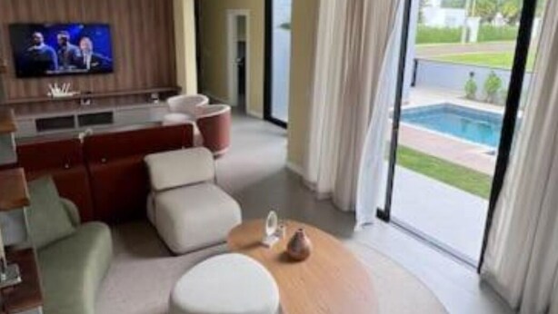 A modern hotel room with a living area featuring a flat-screen TV, a sofa, and a coffee table. The room has a large sliding glass door leading to a pool area. - Elegance Santa Bárbara - Vacation Home at Santa Bárbara Resort Residence (Águas de Santa Bárbara)