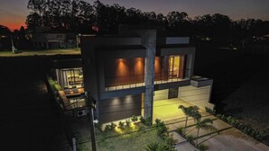 A modern house with a glass facade, a well-lit patio, and a landscaped garden. - Elegance Santa Bárbara - Vacation Home at Santa Bárbara Resort Residence (Águas de Santa Bárbara)
