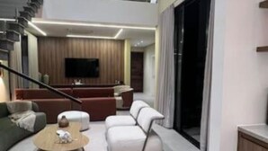 A spacious living area with a high ceiling, a staircase leading to an upper level, a flat-screen TV, and a seating area with sofas and a coffee table. - Elegance Santa Bárbara - Vacation Home at Santa Bárbara Resort Residence (Águas de Santa Bárbara)