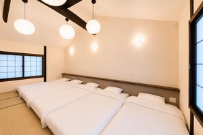 Une chambre d’hôtel avec un lit de style japonais traditionnel, un sol recouvert de tatamis et une fenêtre à panneaux coulissants de type shoji.