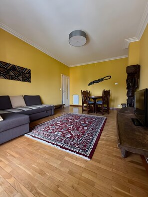 A living room with a sofa, a patterned rug, a dining table with chairs, and a television. - Apartment 'Karibu' with Sea View and Wi-Fi (Sanremo)