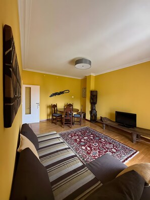 A living room with a sofa, a patterned rug, a dining table with chairs, a TV, and a ceiling light. - Apartment 'Karibu' with Sea View and Wi-Fi (Sanremo)