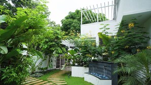 A garden with a stone pathway leading to a white building with a balcony. - ELIVAAS Bauhinia 5 BHK Pvt Pool Villa  (Vagator)
