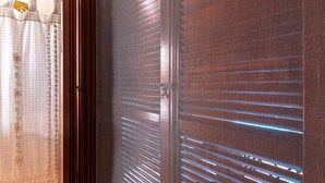 Ein Zimmer mit Fenster, horizontalen Jalousien, einem Vorhang und einer Holztür.