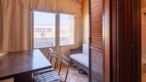 Ein Zimmer mit einem Holztisch, zwei Stühlen, einer Korbschaukel und einem Fenster mit Vorhängen.