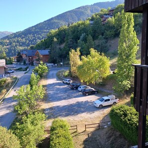 A parking area with vehicles, surrounded by trees and a mountain backdrop.