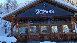 Un bâtiment en bois abritant une station de ski, appelé « SKIPASS », avec une enseigne indiquant « FORFAITS DE SKI ».