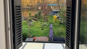 A view through open window shutters of a garden with a lawn, a small pond, and a blue bridge in the background. - villa du beau port (Cenon-sur-Vienne)