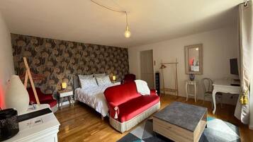 Un dormitorio con una cama, un sofá rojo, una mesa de centro de madera y una alfombra estampada.