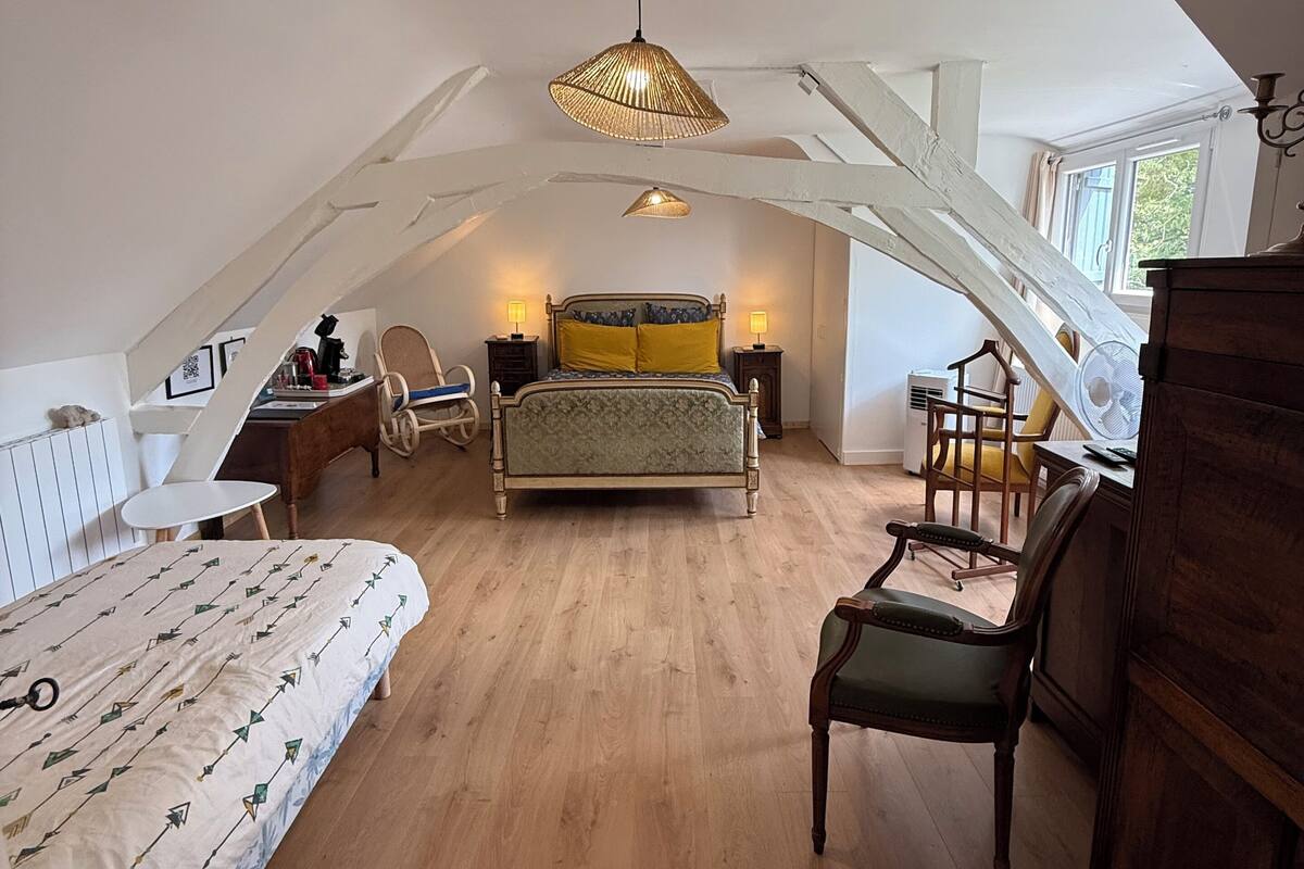 Een slaapkamer met een loft-plafond, een bed met een beddeken met een patroon, een houten stoel, een bureau met een stoel en een hanglamp.