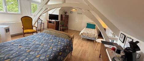 A bedroom with a bed, a desk, a chair, a television, and a window.