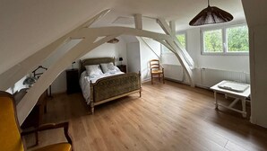 A bedroom with a sloped ceiling, a bed, a chair, a table, and a window with a view of greenery. - villa du beau port (Cenon-sur-Vienne)
