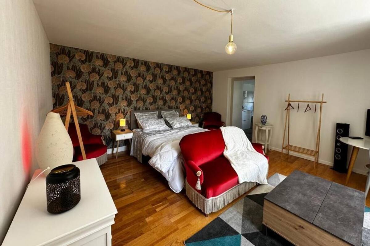 Een slaapkamer met een bed, een rode bank, een tafeltje, een lamp en een speaker.
