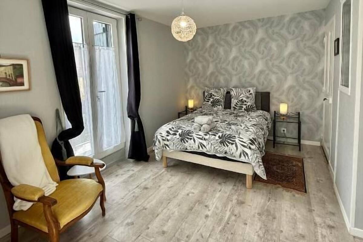 Een slaapkamer met een bed, een stoel, een nachtkastje en een hanglamp.