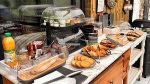 A breakfast buffet with various food items, a clock, and a window view. - villa du beau port (Cenon-sur-Vienne)