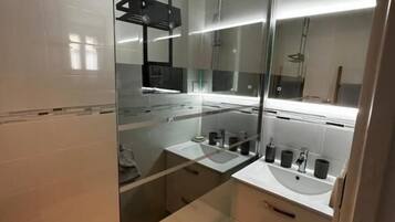 Un baño moderno con cabina de ducha de vidrio, un lavamanos blanco y un espejo grande.