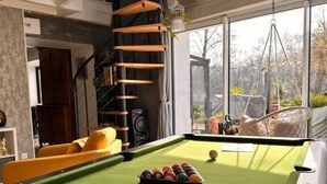 A pool table with balls, a sofa, and a hanging chair in a room with a staircase and large windows. - villa du beau port (Cenon-sur-Vienne)