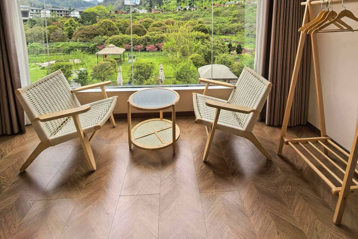 A room with a large window, two wicker chairs, a small round table, and a wooden drying rack.