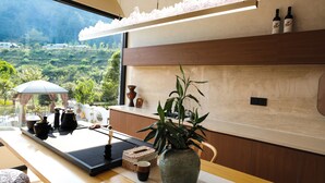 Eine moderne Küche mit Blick auf eine üppige Landschaft, ein Holztisch mit Tee-Service, eine große Vase mit Pflanze und zwei Flaschen an der Wand.