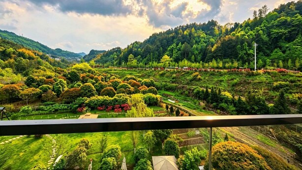 Ein Balkon mit Blick auf ein üppiges Tal, terrassenförmig angelegte Felder und ein fernes Gebirge.