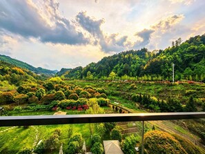 A balcony with a view of a lush valley, terraced fields, and a distant mountain range. - Qipan Yeshe Guesthouse (Zhangjiajie)