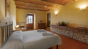 A room with a bed, a desk, a dresser, and a stone wall. - Tenuta Branca – Apartment La Loggia with Pool and Private Terrace in Chianti (San Casciano in Val di Pesa)