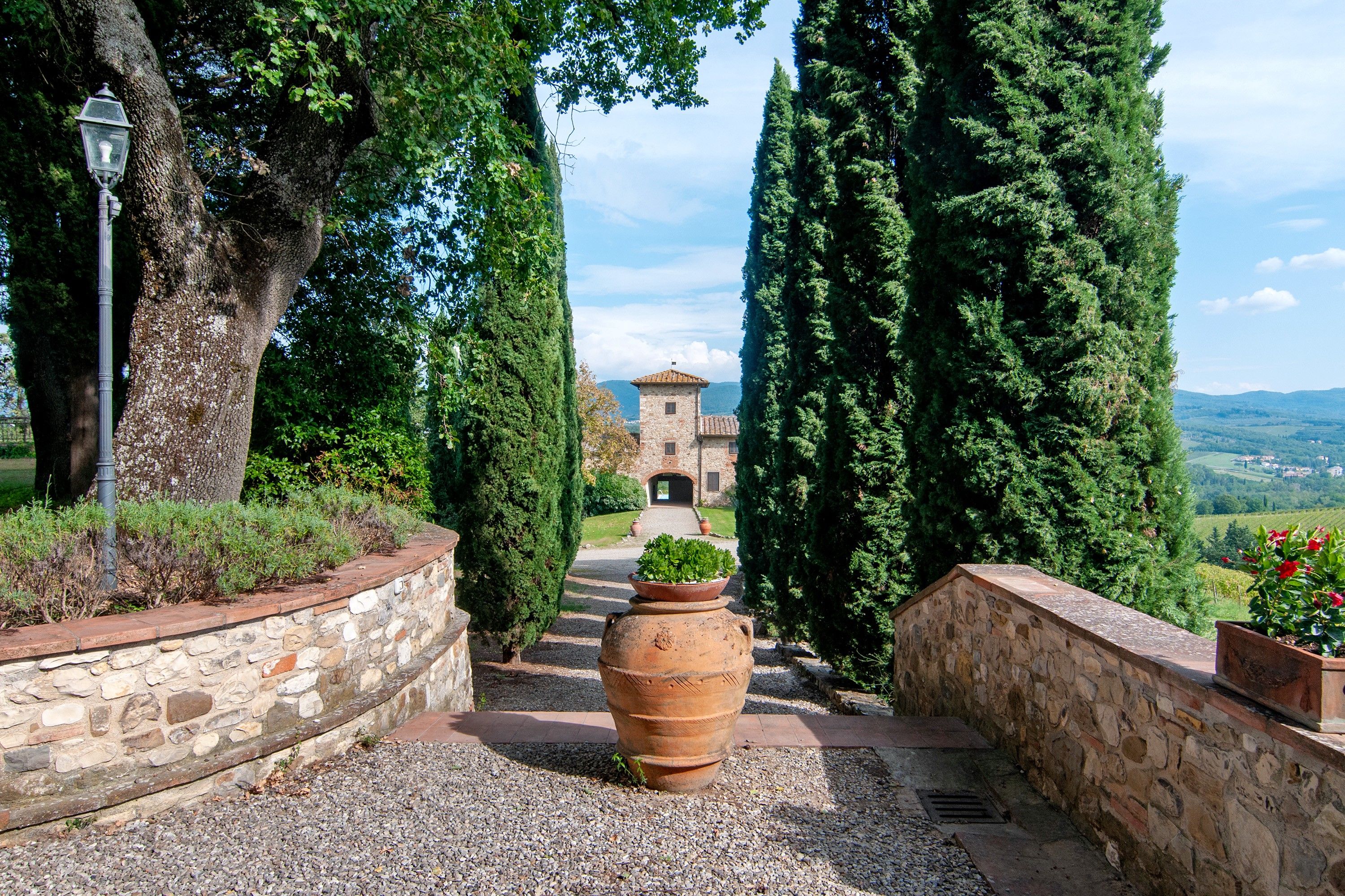 A stone pathway leading to a building with a tiled roof, surrounded by tall cypress trees and a clear sky.