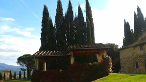 A traditional stone building with a tiled roof, surrounded by well-maintained grass and a row of tall cypress trees. - Tenuta Branca – Apartment La Loggia with Pool and Private Terrace in Chianti (San Casciano in Val di Pesa)