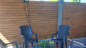 Un patio in legno con quattro sedie di plastica nera e un tavolino intrecciato con una pianta in vaso.