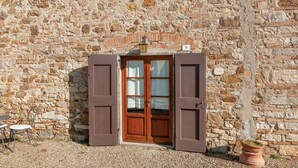 A stone building with a wooden door, a small table with chairs, and a potted plant. - Tenuta Branca - Podere Apartment with Pool and Terrace in Chianti (San Casciano in Val di Pesa)