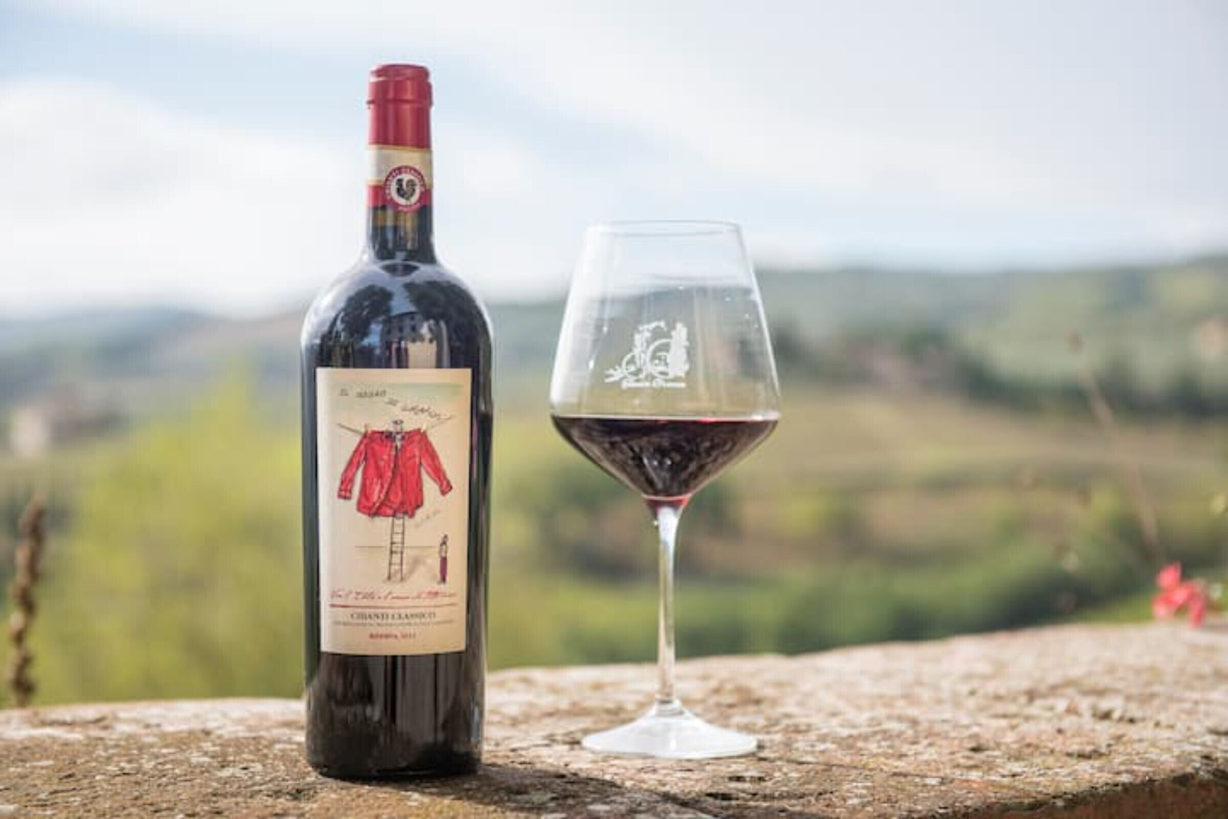 Une bouteille de vin et un verre à vin sur une surface en pierre, avec un paysage flou en arrière-plan.