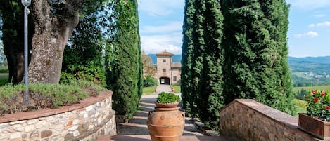 A stone pathway leading to a building with a tiled roof, surrounded by tall cypress trees and a clear sky.