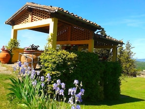 Una estructura tradicional con techo de tejas, rodeada de exuberante vegetación y flores moradas.