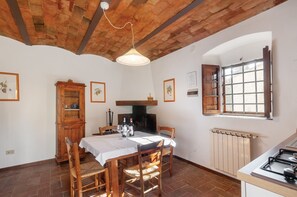 A dining area with a table set for two, a wooden cabinet, a fireplace, and a window with shutters. - Tenuta Branca - Podere Apartment with Pool and Terrace in Chianti (San Casciano in Val di Pesa)