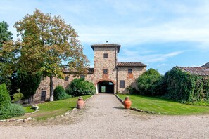 Ein Steinhaus mit einem zentralen Turm, einer Schotterauffahrt und einem gepflegten Garten.