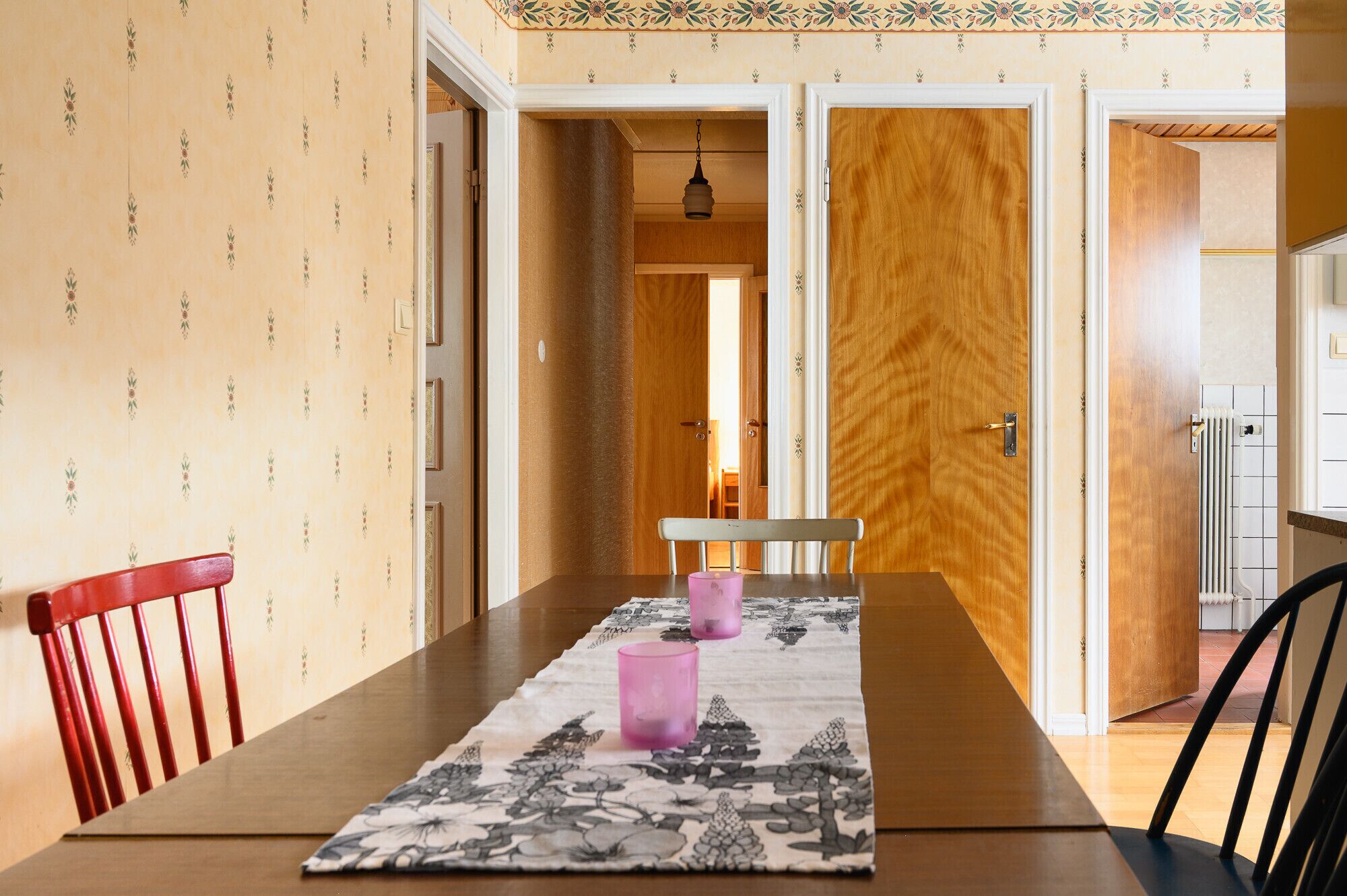 A dining area with a wooden table, two chairs, and a floral table runner.